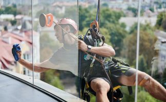 Industrial mountaineering worker cleaning window outside building.